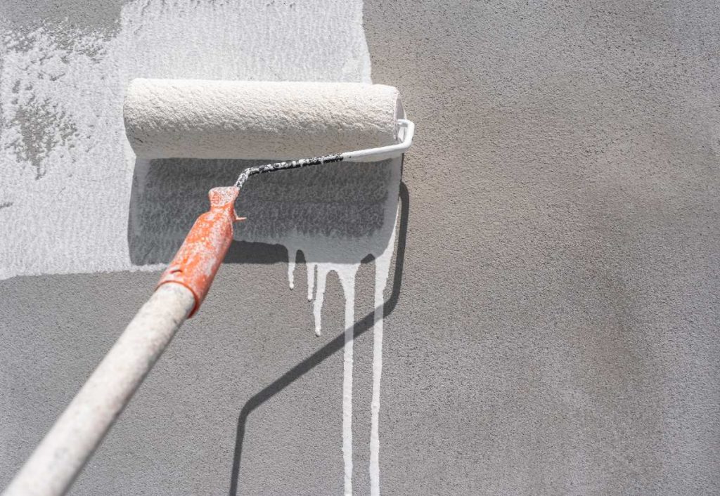 Une personne qui peint la façade extérieure avec un rouleau