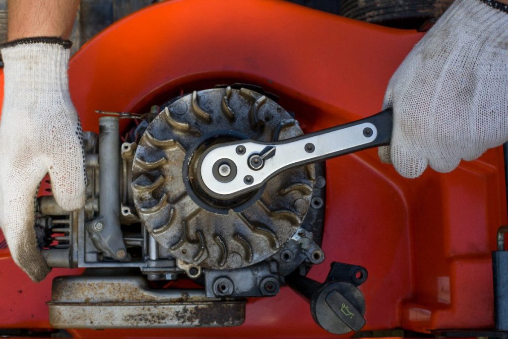 Une personne portant un gant et remplace un lanceur de son motoculteur par un démarreur électrique