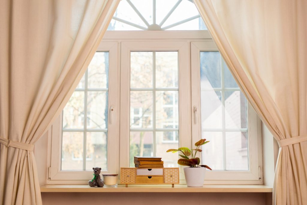 Rideau de couleur beige ouvert sur une fenêtre demi-lune