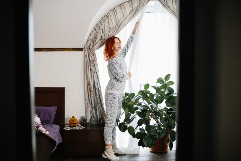 Une femme ouvrant les rideaux sur une fenêtre demi-lune