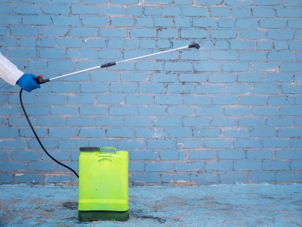 Une personne qui porte un gant et utilise une pompe à détartrer pour nettoyer le mur