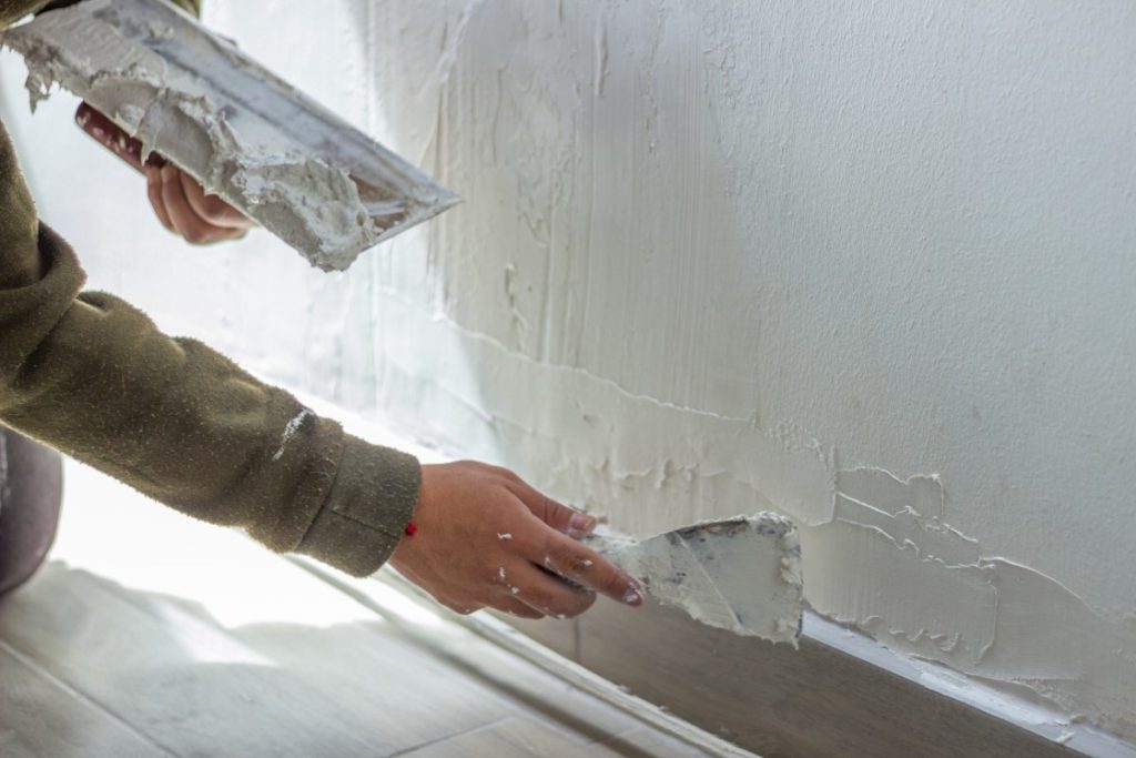 Comment appliquer de l'enduit sur du lambris pour moderniser une pièce ? Un homme appliquant de l'enduit sur le mur