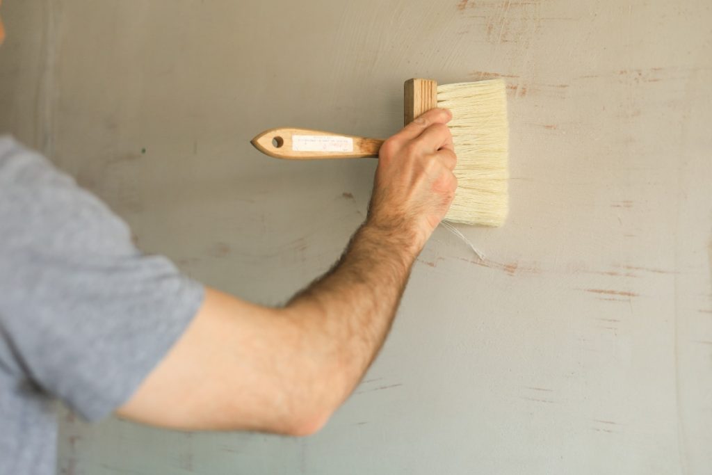 Comment appliquer de l'enduit sur du lambris pour moderniser une pièce ? Un homme qui peint le mur