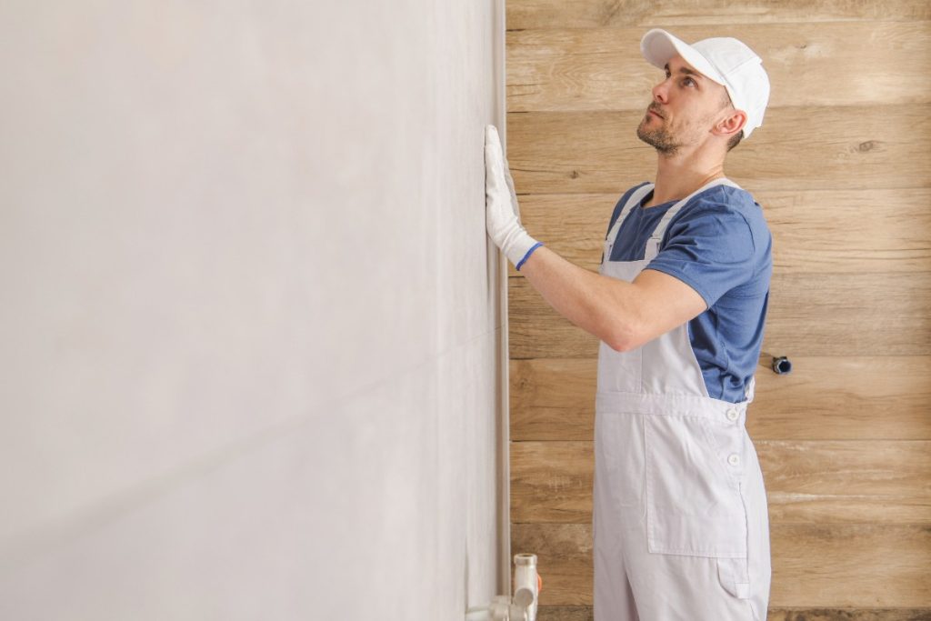 Comment appliquer de l'enduit sur du lambris pour moderniser une pièce ? Un ouvrier lissant du carrelage sur le mur