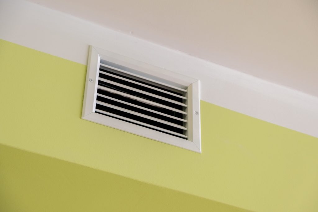 Une grille d'aération blanche sur le mur jaune