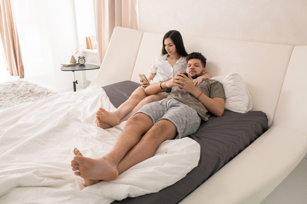 Un jeune couple relaxant au lit avec leur téléphone