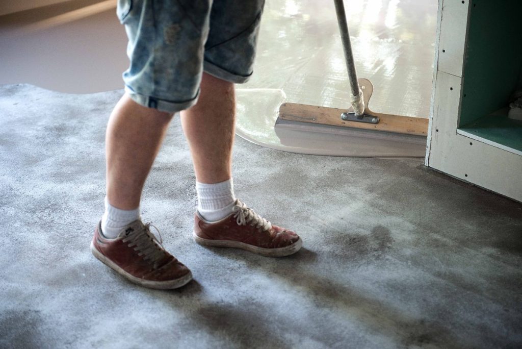 Comment traiter ou recouvrir un sol en terre battue dans une vieille maison ? Un ouvrier qui réalise un nivellement de sols en béton