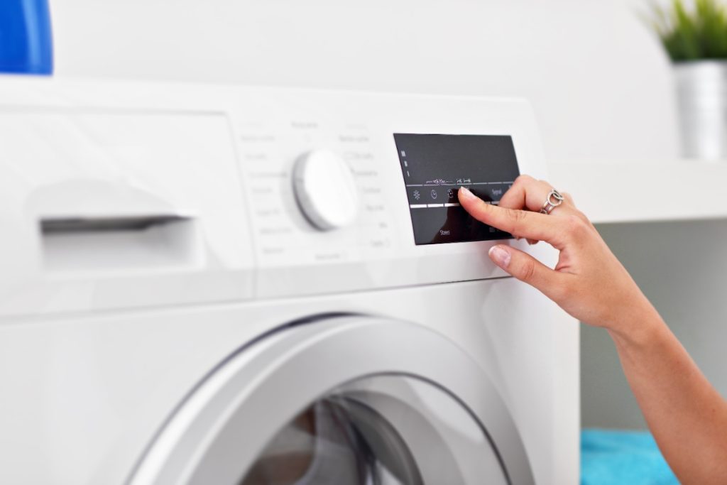 Main d'une femme appuyant sur le bouton d'une machine à laver
