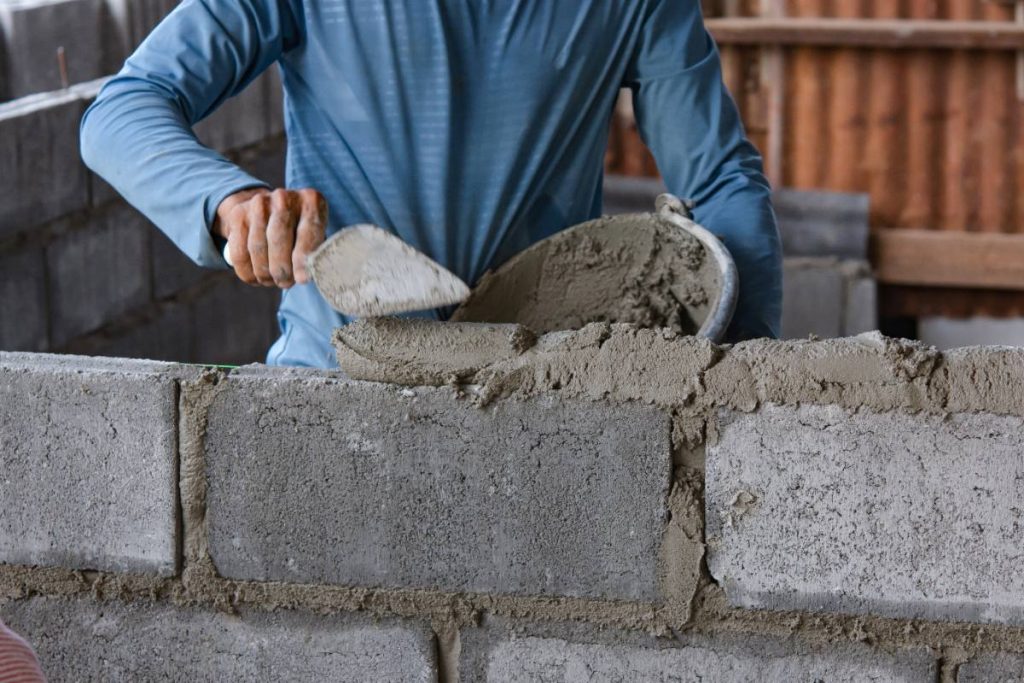 Un ouvrier du bâtiment qui applique du mortier sur des blocs de béton